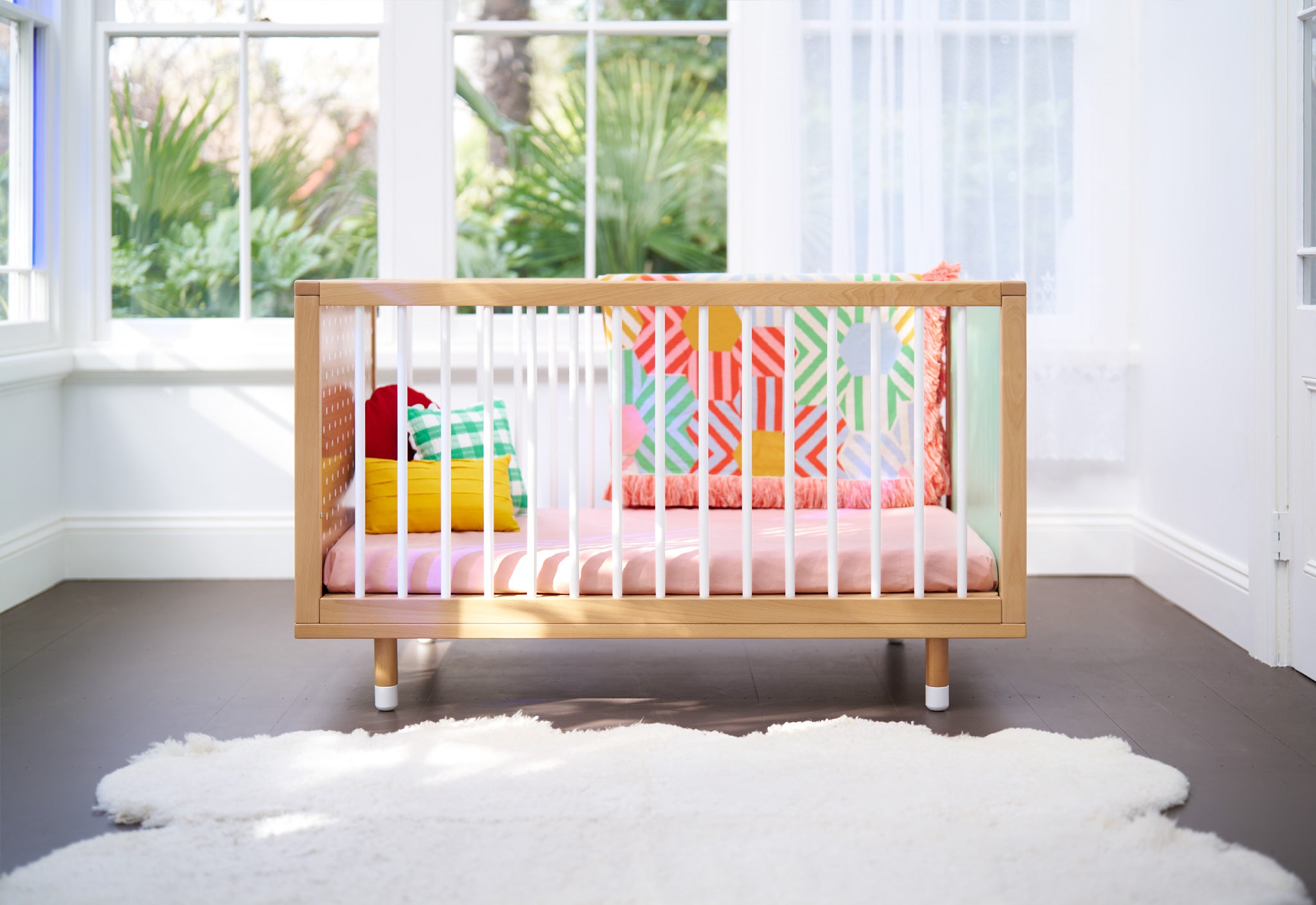 A side view of a cot with colourful blanket and pink sheet